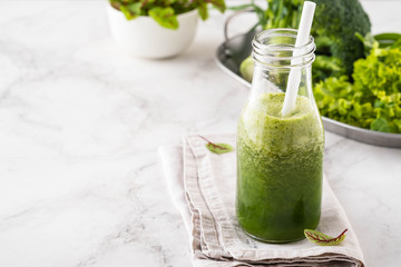 Blended green smoothie with ingredients on the white table.