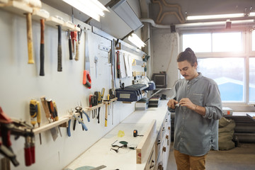 Young worker in casual clothing standing in front of his workplace with work tools and working in workshop
