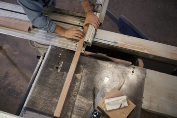 Close-up of young man cutting the wooden plank using lathe during his work in workshop