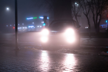 Fototapeta na wymiar the car headlights through the fog, poor and dangerous driving conditions, night time in the city