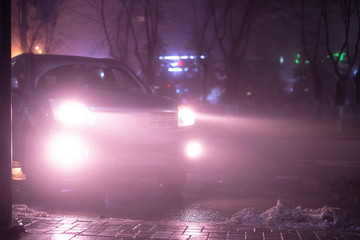 the car headlights through the fog, poor and dangerous driving conditions, night time in the city
