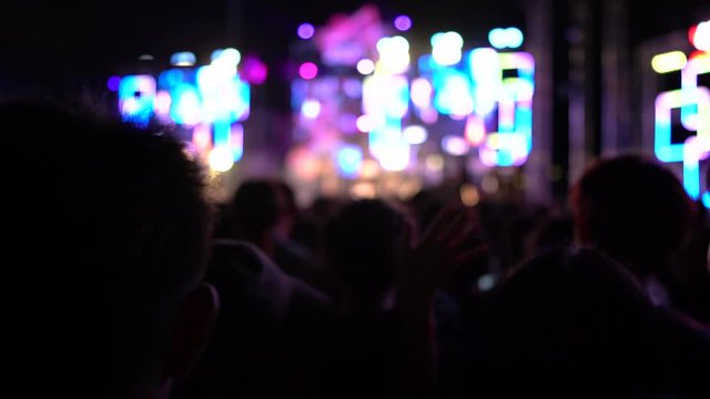 Concert crowd audience people entertainment at night stage lights silhouette raising hands in the music festival rear view with spotlight glowing effect. 4K UHD Footage cinematic blur
