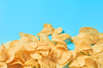 Scattered many fried potato chips on blue background. Space for text