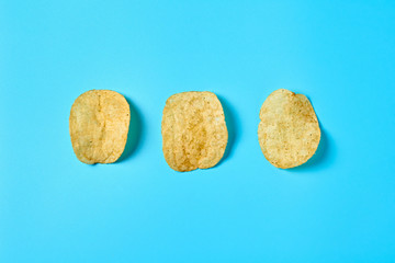 Fototapeta na wymiar Row of three fried potato chips on blue background. Top view. Close-up