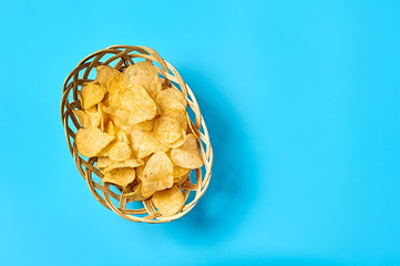 Wooden basket full of spicy fried potato chips on blue background. Space for text. Top view