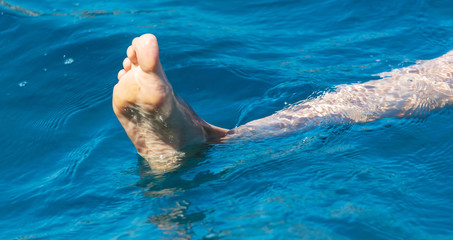 Leg of a girl in the blue water of the sea