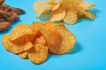 Heaps of snack for beer spicy potato chips, pieces of rusk bread lies on blue table in sport bar or pub. Close-up