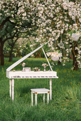 White wooden piano with stool and romantic decor surrounded by blooming Apple trees in the spring...