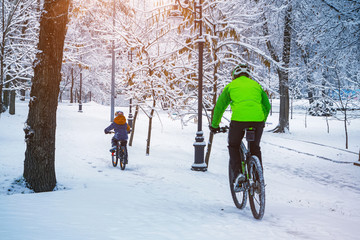 A father and his son ride a bikes in a winter park