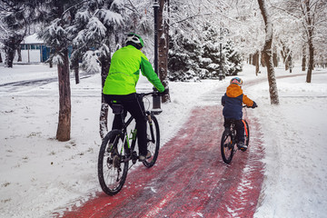 Man and his son ride bicycles along a bicycle path in a winter park
