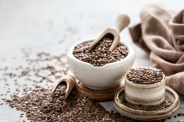 Flax seeds in a ceramic bowl with a wooden spoon on a white background. Organic healthy food