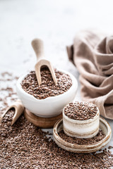 Flax seeds in a ceramic bowl with a wooden spoon on a white background. Organic healthy food