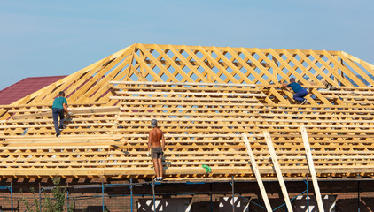 Workers are building the roof of the house from wood