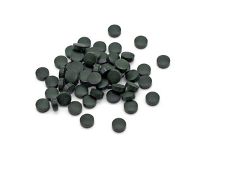 Dark green round pills lie in a pile on a white background. Selective focus