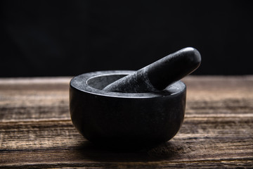 Pestle and mortar with black stone on wooden table - obrazy, fototapety, plakaty