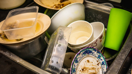 Dirty dishes, utensil, plastic container and food waste piled in a metal sink at the kitchen.