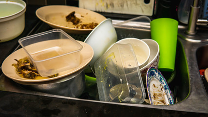 Obraz na płótnie Canvas Dirty dishes, utensil, plastic container and food waste piled in a metal sink at the kitchen.