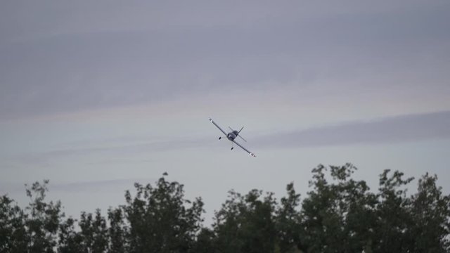 A small homebuilt airplane turns to face the camera head-on over some tall trees.
