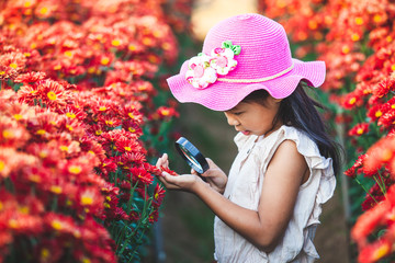 Cute asian child girl looking beautiful flower through a magnifying glass in the flower field