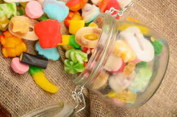 Multicolored shaped marmalade in a glass jar on a background of rough homespun fabric close-up. Delicious holiday treat.