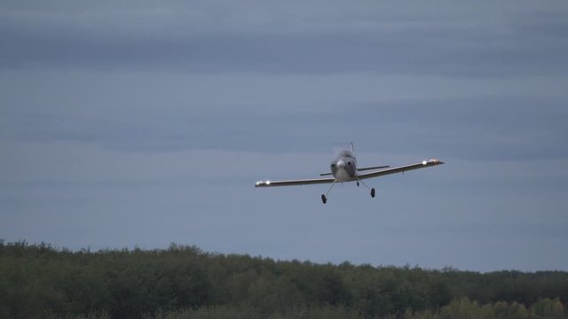 A small homebuilt airplane flies over a runway and toward the camera in slow motion.
