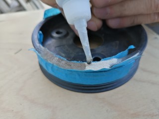applying liquid glue to a car pulley from a plastic container in hands on a wooden background