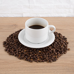 cup of coffee with coffee seeds on wooden table and light brick background