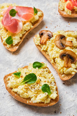 Scramble omelet sandwiches, bacon, mushrooms, tomatoes and fresh herbs on a light gray background.