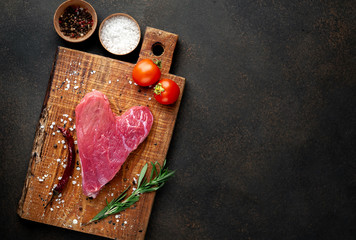 heart shaped raw beef steak on a cutting board with spices for valentines day on a stone background with copy space for your text, concept of cooking dinner for valentines day