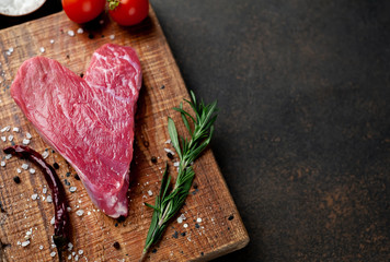 heart shaped raw beef steak on a cutting board with spices for valentines day on a stone background with copy space for your text, concept of cooking dinner for valentines day