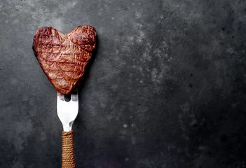 Tuinposter Gegrilde biefstuk in de vorm van een hart op een vork voor Valentijnsdag op een stenen achtergrond met kopieerruimte voor uw tekst © александр таланцев