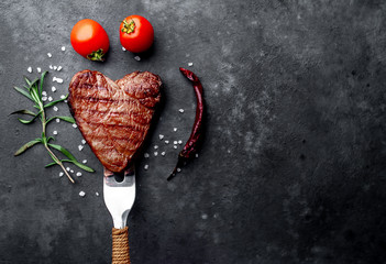 grilled beef steak in the form of a heart on a fork for Valentine's day on a stone background with...