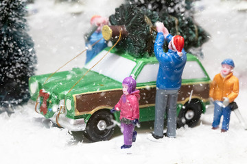 Miniature people in christmas. The family loads the tree on the car.
