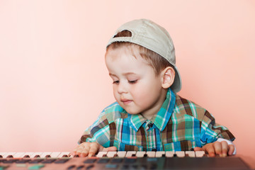 Portrait of a pretty boy wearing baseball cap backwards playing the digital piano.