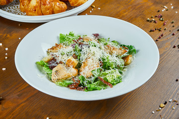 Caesar salad with croutons, parmesan, chicken, egg in a black stylish bowl. Restaurant serving. Selective focus, wooden background