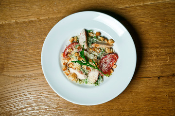 Caesar salad with croutons, parmesan, chicken, egg in a black stylish bowl. Restaurant serving. Selective focus, wooden background
