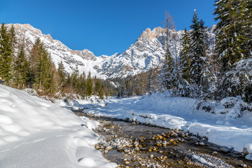 Sunny winter landscape in the alps: Mountain range, river, snowy trees, sunshine and blue sky