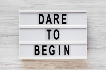 'Dare to begin' words on a modern board on a white wooden surface, top view. Overhead, from above,...