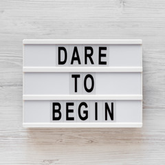 'Dare to begin' words on a modern board on a white wooden background, top view. Overhead, from...