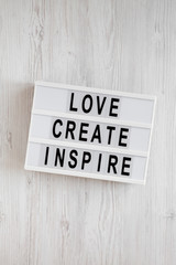 'Love create inspire' words on a modern board on a white wooden background, top view. Overhead, from above, flat lay.