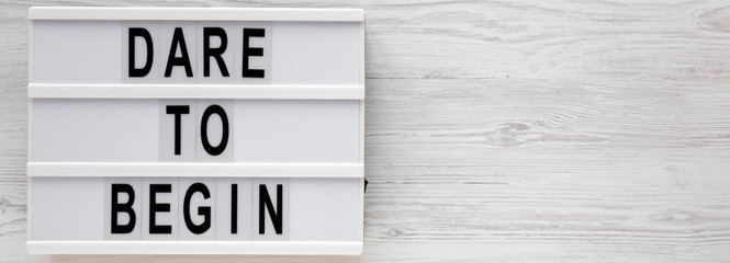 Obraz premium 'Dare to begin' words on a modern board on a white wooden surface, top view. Overhead, from above, flat lay. Copy space.