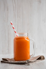 Homemade Mango Carrot Smoothie in a glass jar mug over white wooden surface, side view. Close-up.
