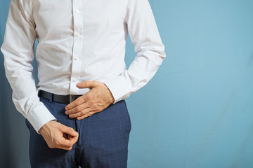 A man in trousers and a white shirt holds on to the lower abdomen and unfastens his fly, signs of...