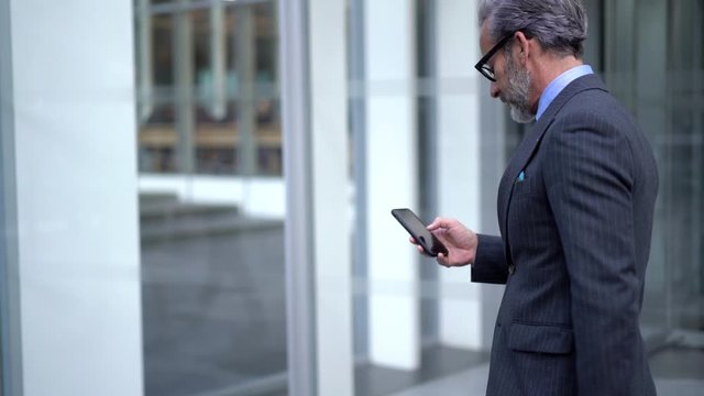 Slow motion effect of successful middle aged businessman dressed in luxury suit using 4g internet for online messaging via cellphone device, confident entrepreneur chatting and using online banking ap
