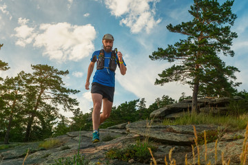 Naklejka premium Athlete jogging among the rocks in a beautiful natural place. Man in blue jersey and black shorts training outdoors