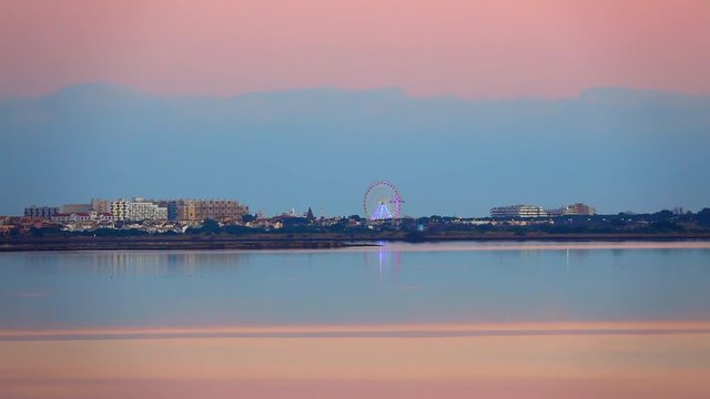 View from the lake to the night seaside city with tall buildings and entertaining attractions at sunset painted in blue and pink. Leucate, France