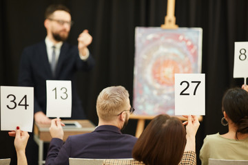 Rear view of group of business people with signs buying a painting during the auction - obrazy, fototapety, plakaty