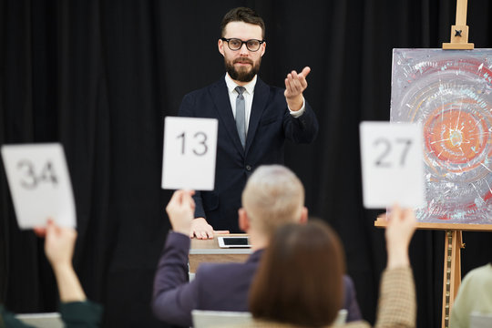 Young businessman in suit standing and pointing at candidate who wants to buy a painting at auction