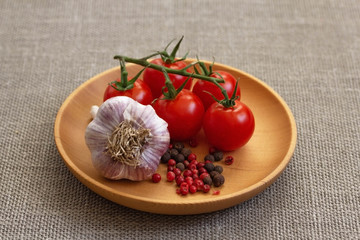 Cherry tomatoes, garlic and pink pepper closeup in a wooden plate on a gray burlap background. Food background. Photo of food side view, wooden dishes.