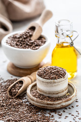 Flaxseed oil in a bottle and ceramic bowl with brown flax seeds and wooden spoon on a white background. vertical.